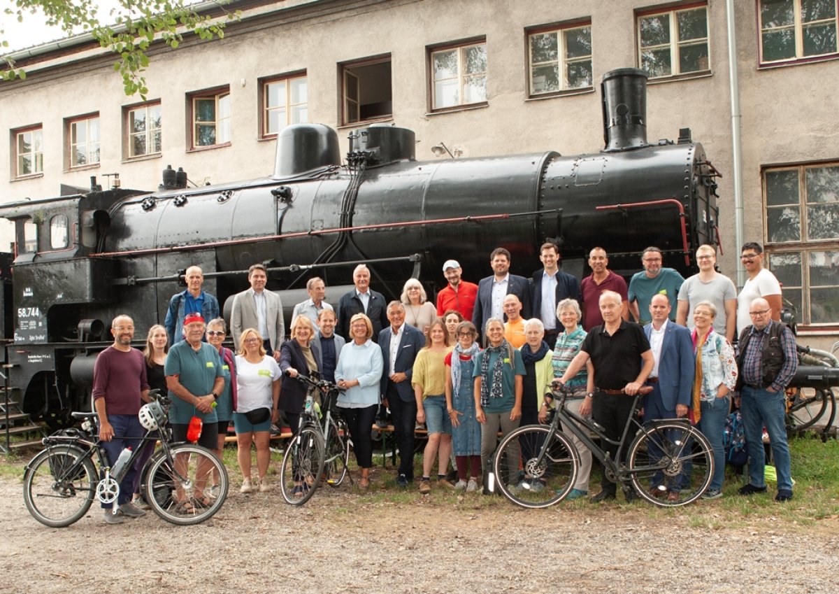 Einst eine Bahntrasse – nunmehr seit 20 Jahren eine Radroute: Der Dampfross und Drahtesel Radweg hat dieses Jahr sein 20 jähriges Jubiläum. Aus diesem Anlass lud die ARGE Dampfross und Drahtesel am 31.8.2025 nachmittags zur Jubiläumsfeier ins Eisenbahnmuseum und Heizhaus Strasshof an der Nordbahn, einer der Attraktionen an der Route. Die Feier fand im Rahmen des jährlichen Kinderfestes des Heizhauses statt. Wer mit dem Rad kam, hatte freien Eintritt. Fünf der lokalen Radlobby Gruppen aus der Umgebung – Deutsch Wagram, Gänserndorf, Wolkersdorf sowie Wien Donaustadt und Wien Floridsdorf organisierten eine Sternfahrt mit dem Rad zur Feier. Insgesamt wurden zum Zeitpunkt der Feier 56 Radlerinnen (davon 10 Kinder) gezählt.  Durch das Programm führte STR Christian Schrefel (Wolkersdorf). Nach der Begrüßung durch BGM Ludwig Deltl (Strasshof a.d.Nordbahn) wies Museumsleiter Rupert Gansterer auf die Möglichkeit einer Museumsbahn am Schweinbarther Kreuz hin. ARGE Obfrau Alexandra Nürnberger betonte die gute Zusammenarbeit in der ARGE und die aktiven Partnergemeinden die regelmäßig den Radweg pflegen.  Die anwesenden Landtagsabgeordneten Klubobfrau Helga Krismer und Georg Ecker (beide Die Grünen) sowie Rene Zonschitz (SPÖ) betonten die Wichtigkeit des Radfahrens und die Unterstützung des Landes beim Ausbau der Radinfrastruktur über das NÖ Radbasisnetz. Anschließend erzählten die langjährige ARGE Leiterin Sylvia Gleitsmann und Gründungsmitglied Alt-BGM Wolfgang Gössinger (Pillichsdorf) mit launigen Worten und Anekdoten über den Werdegang der Radroute.  STR Christian Schrefel interviewte aktuelle und ehemalige Bürgermeister und Gemeinderäte der ARGE Gemeinden, sowie den Obmann von Weinviertel Tourismus Hannes Steinacker und Radlobby Wolkersdorf Obmann Hermann Hiebner. Alle sprachen die die Wichtigkeit guter Radinfrastruktur für den Alltags- und Freizeitverkehr an, insbesondere in Zeiten des Klimawandels. Hervorgehoben wurde die Wien und das Weinviertel verbindende Lage des Dampfross und Drahtesel Radweges. Diese wurde nun ergänzt durch die Eröffnung einer neuen Variante, einer direkten Verbindung von Gerasdorf nach Pillichsdorf. Durch die Beschilderung eines Alltagradweges zur U2 Station Leopoldau (und weiter ins Zentrum von Wien) gewinnt diese Strecke an zusätzlicher Bedeutung. Abgerundet wurde die Veranstaltung mit der Vergabe der ehemaligen Radwegschilder an die Anwesenden: die alte Beschilderung, das Logo der Route auf weißem Hintergrund, war in den vergangenen Monaten im Zuge des Neubeschilderungsprogrammes durch Weinviertel Tourismus abmontiert worden und durch Schilder nach dem Neuen Niederösterreich Standard (grün) ersetzt. 